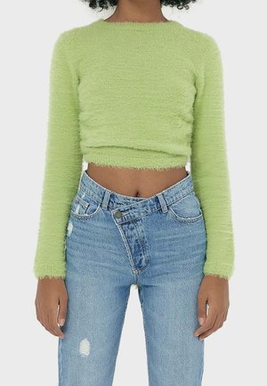 Sweater court à manches longues vert clair en matériau doux et pelucheux. Associé à un jean taille haute bleu clair déchiré avec une fermeture à boutons.