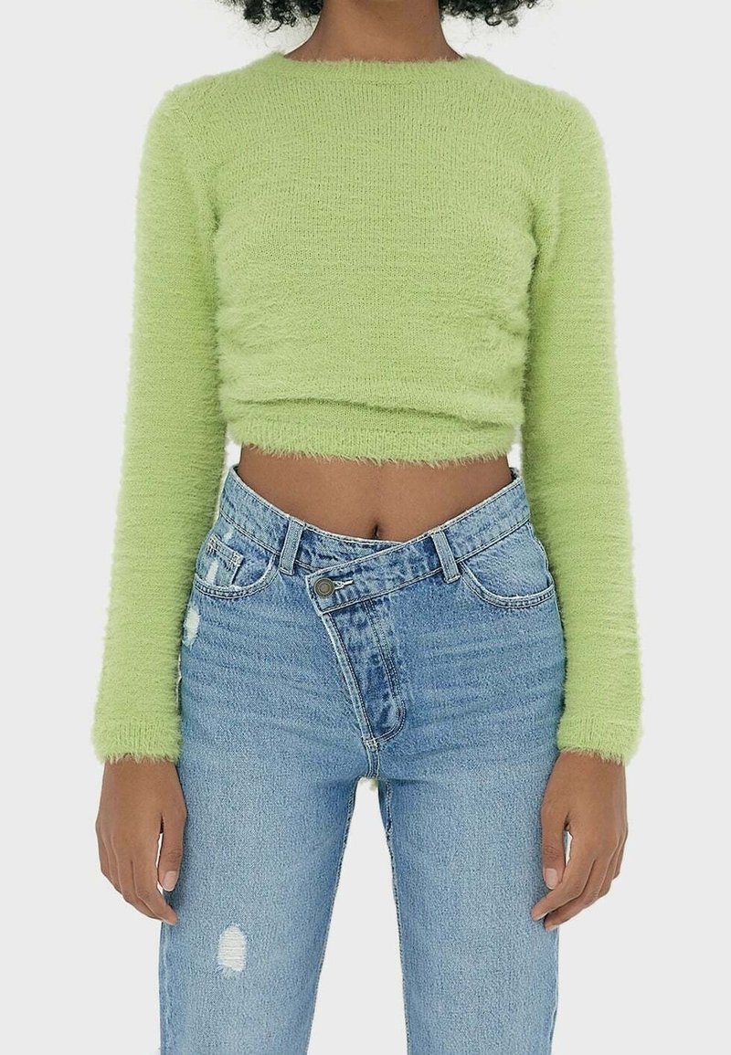 Sweater court à manches longues vert clair en matériau doux et pelucheux. Associé à un jean taille haute bleu clair déchiré avec une fermeture à boutons.