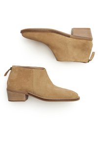 Botas de ante color beige hasta el tobillo con punta afilada, tacón bajo apilado y detalle de cremallera en la parte trasera. Textura lisa y costura a lo largo de la suela.