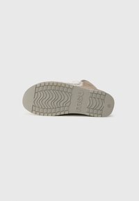 Sole din cauciuc gri, cu un model texturat, ce include logo-ul brandului. Materialul superior pare moale, având o culoare bej deschis și cusături decorative.