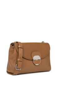 Brun skuldertaske i pebret læder med flaplukning, sølvfarvede beslag og justerbar rem. Har en fremtrædende cirkulær detaljer.