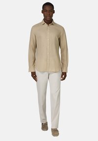 Camicetta beige chiaro a maniche lunghe realizzata in un tessuto testurizzato, con chiusura frontale a bottoni. Abbinata a pantaloni chiari e calzature casual.