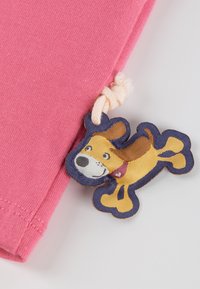 Pink cotton fabric with a woven label featuring a playful dog design in yellow and brown, accented with a light rope tie.