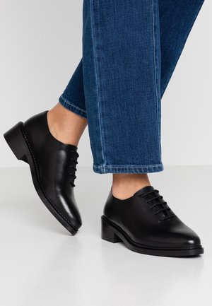 Sorte læder snøresko med rund tå, lav blokhæl og syningsdetaljer, båret med cropped blå jeans.