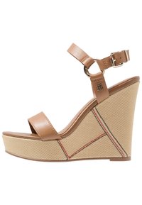Sandale à talon compensé avec une sangle en cuir tan, boucle réglable à la cheville et une plateforme en tissu beige texturé avec des accents de couture rouges.