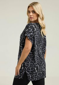 Top de estampado de leopardo en negro y gris con mangas cortas, dobladillo redondeado y aberturas laterales. Hecho de una tela ligera y texturizada, adecuada para superponer.