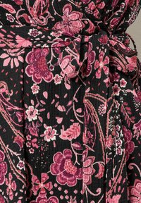 Tessuto nero con un motivo floreale in rosa, viola e bianco. Presenta una vita legata e una superficie strutturata.