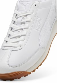 White leather sneaker with textured surface, thin laces, and a gum rubber sole. Features subtle branding on the side and padded collar.