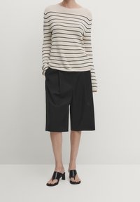Maglione a righe beige e nero, vestibilità ampia, abbinato a pantaloni corti neri fino al ginocchio e sandali neri con tacco a blocco e open-toe.
