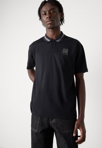 Zwarte polo shirt met grijze accenten, korte mouwen en een kraag. Bevat een logo op de borst en een gladde, gestructureerde stof.