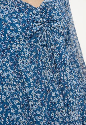 Abito floreale blu con dettagli arricciati sul collo, tessuto leggero e un design fluido con piccoli motivi floreali ripetitivi.