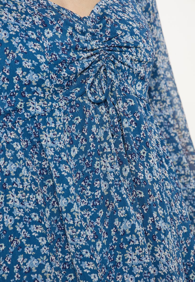 Blå blommig klänning med samlad detalj vid halsringningen, lättviktsmaterial och en flödande design med små, upprepande blommönster.