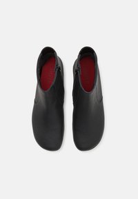 Paire de bottines en cuir noir avec fermetures éclair latérales et semelles intérieures rouges, vues de dessus sur fond clair.