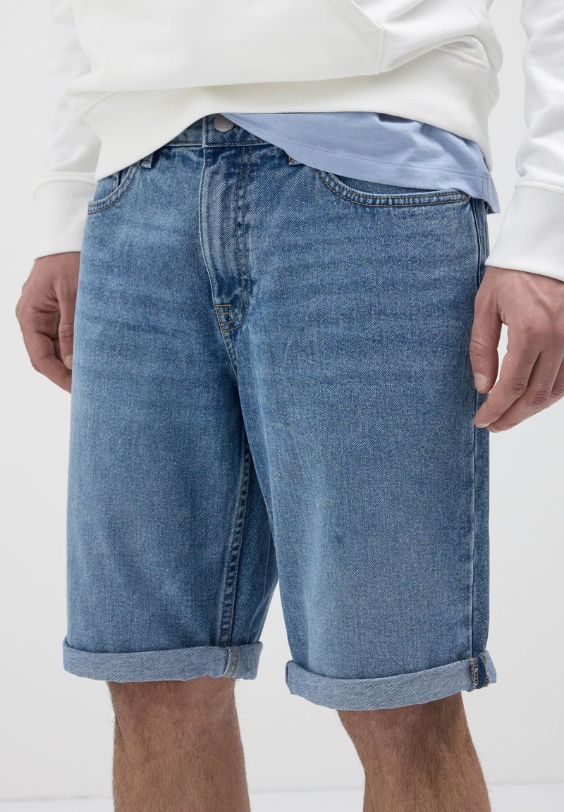 Shorts en denim bleu clair avec une finition légèrement délavée, présentant des revers, un design à cinq poches et une fermeture à bouton.