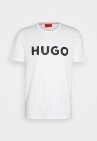 Biała koszulka z krótkim rękawem z wyraźnym czarnym napisem "HUGO" umieszczonym na środku klatki piersiowej oraz widoczną czerwoną metką wewnątrz kołnierza.