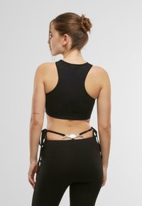 Svart kortermet tanktopp med rund hals, med en glatt tekstur, og kombinert med høyt liv leggings som har knyte-detaljer og dekorativt tilbehør.
