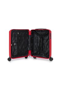 Valise rigide rouge avec un extérieur texturé, fermetures à glissière, et un intérieur présentant un revêtement noir avec un motif à rayures blanches et des sangles élastiques.