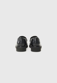Black leather shoes with a smooth finish, rounded design, and low, block heels. Features simple stitching and a minimalistic style.