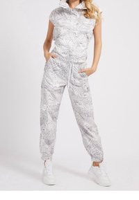 Combinaison légère à capuche avec un motif texturé de feuilles grises et blanches ; taille élastique et chevilles resserrées ; associée à des baskets blanches.