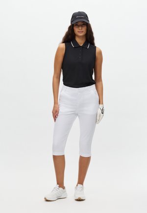 Czarna bezrękawnikowa koszulka polo z białym kołnierzykiem, białe spodnie do połowy łydki oraz białe buty sportowe. Trzyma rękawiczkę golfową, ma na głowie czarną czapkę.