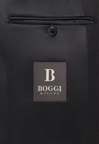 Juodas audinys, ant kurio yra mygtukas su įspaustu žodžiu "BOGGI". Stačiakampė etiketė skelbia "BOGGI MILANO", su ryškiu baltu raide "B".