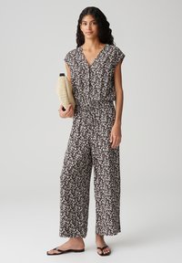 Tuta con motivo floreale in bianco e nero, con scollatura a V, maniche corte e vestibilità comoda. Il modello tiene una borsa a tracolla intrecciata color sabbia.