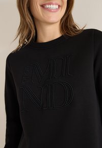 Czarny sweatshirt z wytłoczonym napisem "open MIND" w ciemnym kolorze. Materiały obejmują gładką tkaninę o kroju z okrągłym dekoltem.
