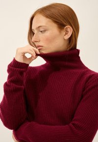 Burgundowy sweter z golfem o ryfrowanej fakturze, z długimi rękawami i wysokim kołnierzem, cechujący się luźnym krojem i miękkim, wełnianym wyglądem.