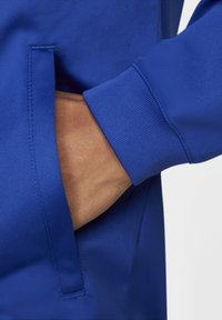 Blå sweatshirt har et struktureret stof og en sidelomme. Ærmerne er ribbede, hvilket giver en tæt pasform omkring håndleddet.