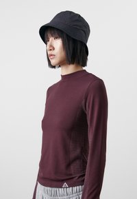 Mörkröd långärmad topp i texturerad tyg med prickiga detaljer på ärmarna. Matchad med en svart bucket hat. Triangel-logotyp vid nederkanten.