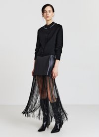 Schwarze Strickjacke mit Knöpfen, verziertem Ausschnitt, kombiniert mit einem schwarzen Minirock aus Leder und Fransen am Saum. Schwarze spitze Stiefel vervollständigen den Look.