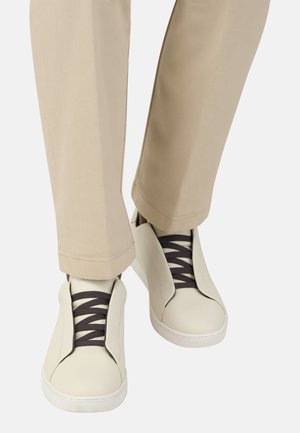 Hvide lædersneakers med mørke elastiklisser, med en slip-on-design og minimalistisk form. Kombination med tan, bukser med lige ben.