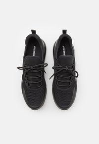 Svarta sportskor med ovandel av nät, designade med rund tå, snörning och en kraftig sula för stöd. Enkel och stilren finish.
