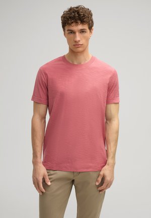 T-shirt a maniche corte, con scollo rotondo, in tessuto rosa testurizzato, caratterizzato da una vestibilità comoda e dettagli di design sottili. Abbinato a pantaloni beige.