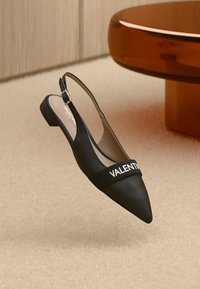 Mustad slingback tasapõhi, millel on terav nina ja paks valge riba tekstiga "VALENTINO". Ühtlane nahkmaterjal minimalistliku disainiga.