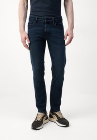 Dark blue denim jeans with a slim fit, featuring front pockets and subtle stitching details, paired with dark sneakers and a black shirt.