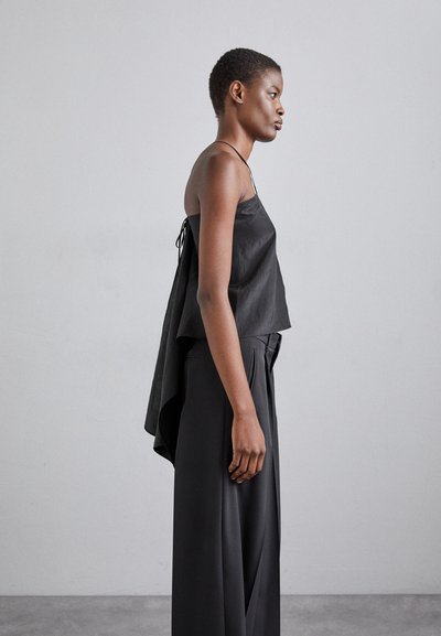 Black sleeveless top with a loose fit, featuring a draped back and thin straps. Paired with high-waisted black trousers. Smooth texture.
