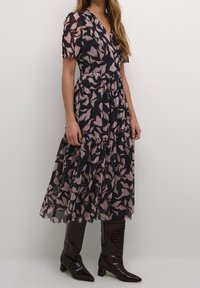 Polven mittainen musta mekko, jossa on kukkakuvio ja vaaleanpunaisia lehtiä. Valmistettu läpikuultavasta kankaasta, lyhyillä hihoilla ja monikerroksisella hameosalla.