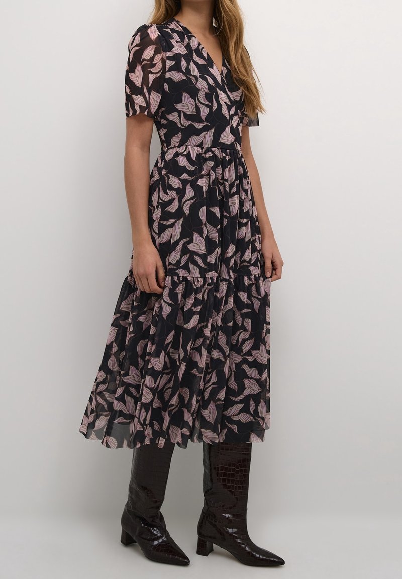 Polven mittainen musta mekko, jossa on kukkakuvio ja vaaleanpunaisia lehtiä. Valmistettu läpikuultavasta kankaasta, lyhyillä hihoilla ja monikerroksisella hameosalla.