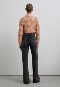 Blusa larga de manga larga de un suave durazno, con volantes, combinada con unos jeans de cintura alta en gris oscuro que presentan bolsillos traseros y una textura sutil.