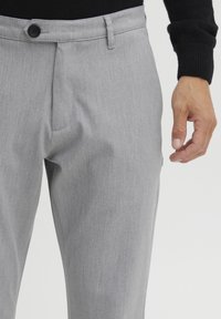 Pantalones a medida gris hechos de una tela texturizada. Presentan un cierre frontal con botón y bolsillos inclinados, con un diseño elegante de pierna recta.