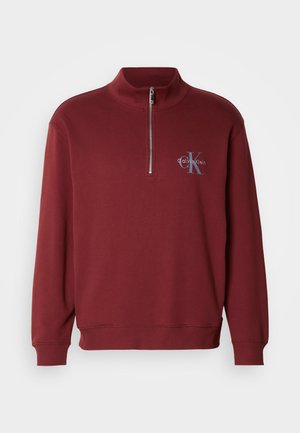Bordowy sweatshirt z ćwierć zamkiem, wykonany z miękkiego materiału, z długimi rękawami, ściągaczami przy nadgarstkach oraz detalem logo na klatce piersiowej.