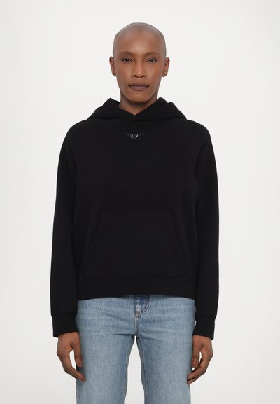Black hoodie with a kangaroo pocket, soft texture, raglan sleeves, and a small logo detail on the chest; paired with light blue jeans.
