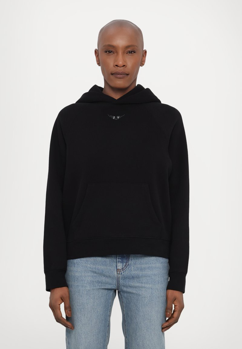 Svart hettegenser med kengurulomme, myk tekstur, raglanermer og en liten logodetalj på brystet; kombinert med lyseblå jeans.