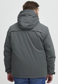 Grå hettejakke med en glatt, matt overflate. Har elastiske mansjetter og en rett kutt. Minimalistisk design, egnet for lagdeling.