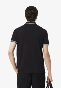 Svart polo-shirt med klassisk krage, korta ärmar och randiga accenter vid kragen och ärmsluten. Materialet verkar smidigt och lätt.