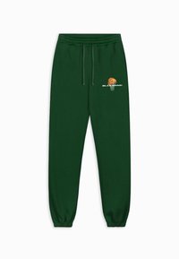 Groene trainingsbroek met een elastische tailleband en boorden, voorzien van een geprinte basketbalafbeelding en logo op de linkerdij. Zachte stoftextuur.