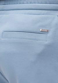 Poche en tissu bleu clair avec une fente horizontale et une petite étiquette rectangulaire en métal de la marque Michael Kors en haut à droite.