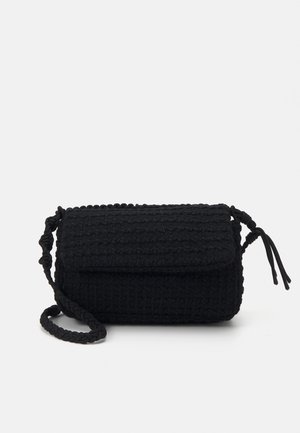 Sac bandoulière noir texturé avec sangle tressée et fermeture à rabat, doté de détails noués aux extrémités de la sangle.