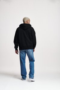 Sudadera con capucha negra de corte relajado, combinada con jeans rectos de un azul claro. El modelo está de espaldas, mostrando la vista trasera.